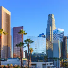 Downtown Los Angeles skyline with modern skyscrapers and palm trees under a clear blue sky.