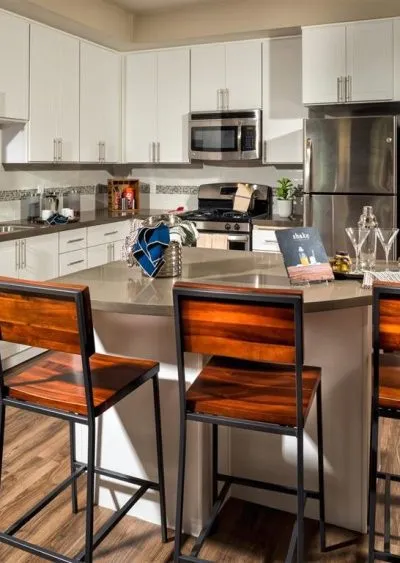 Modern kitchen with white cabinets, stainless steel appliances, and wooden barstools at an island.