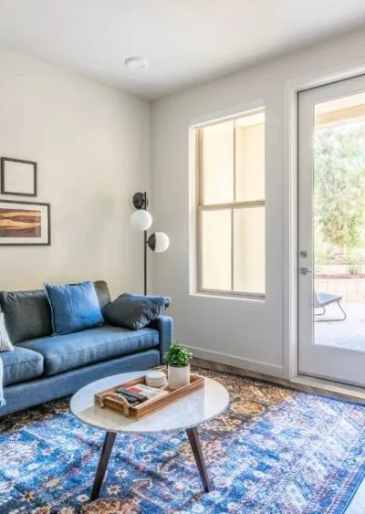 A modern living room with a blue sofa, marble coffee table, and large window with natural light.