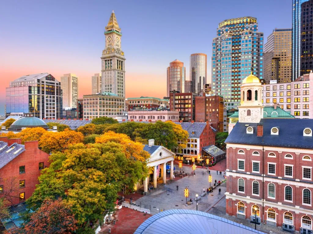 Boston skyline at sunset with historic Faneuil Hall and modern skyscrapers in the background.