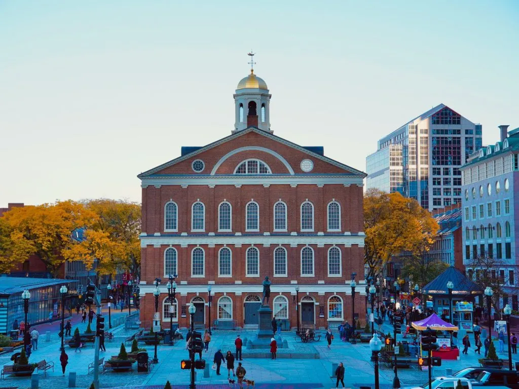 Faneuil Hall in Boston, surrounded by autumn trees and bustling pedestrian activity.