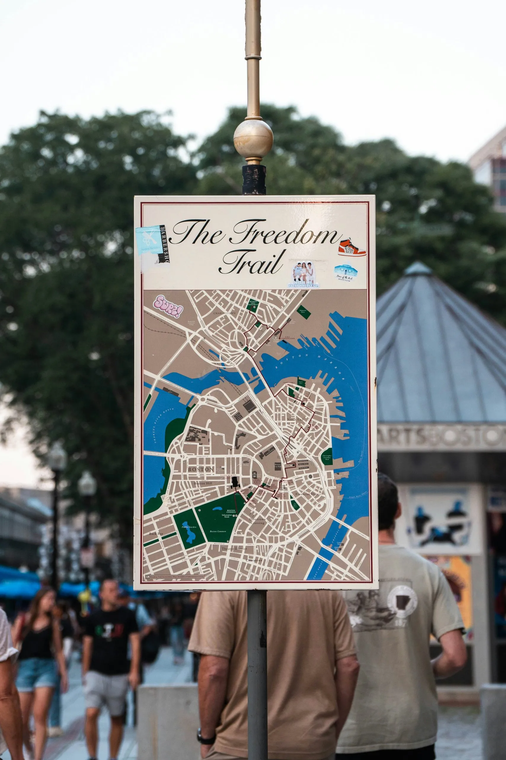 A sign displays a map of Boston's Freedom Trail, surrounded by pedestrians and urban scenery.