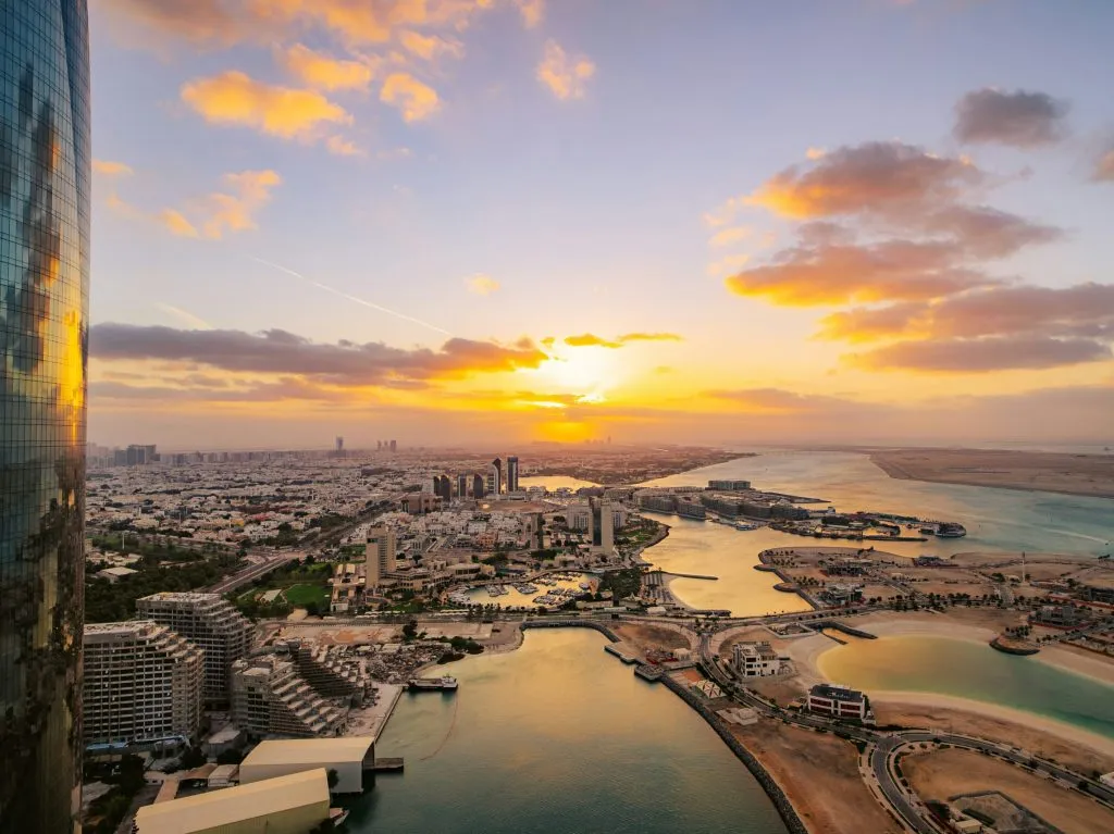 A coastal cityscape at sunset, featuring modern architecture, waterways, and vibrant skies.
