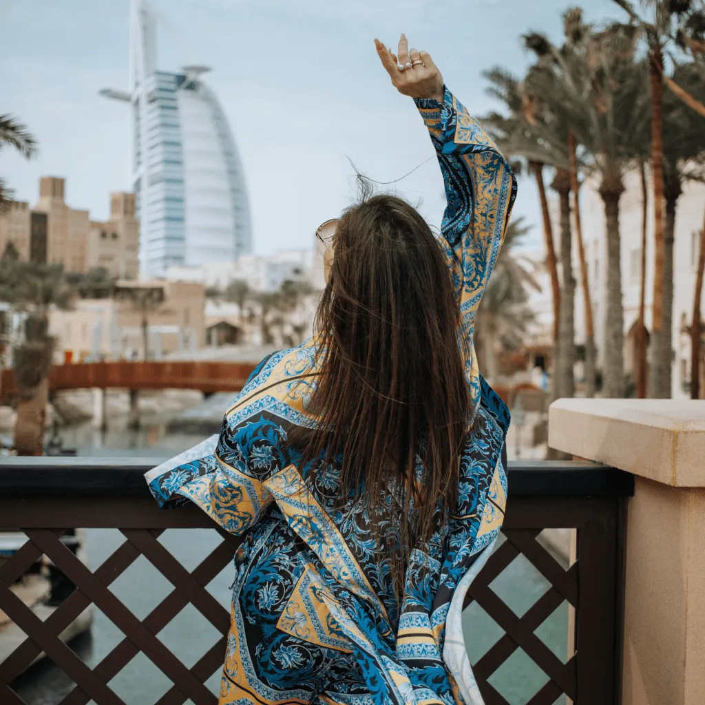 Woman in a patterned blue and yellow outfit poses on a bridge with Burj Al Arab in the background.