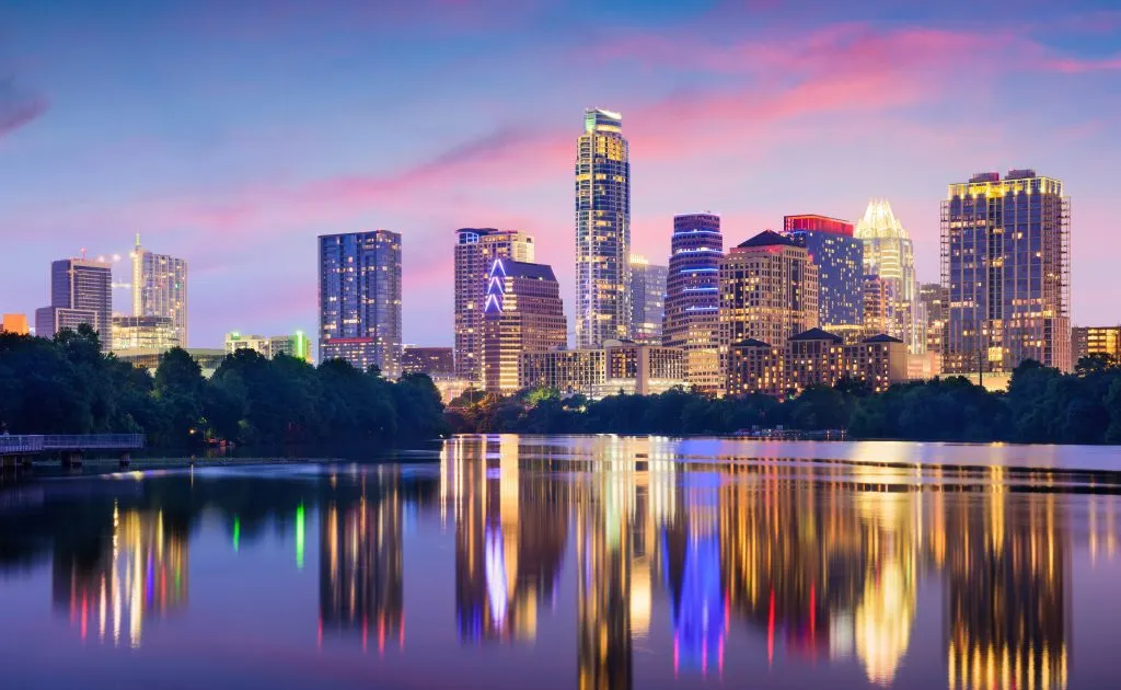Austin skyline at dusk, reflecting vibrant lights on the calm waters of Lady Bird Lake.