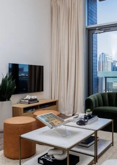 Modern living room with a green armchair, TV, marble coffee table, and city view through glass doors.