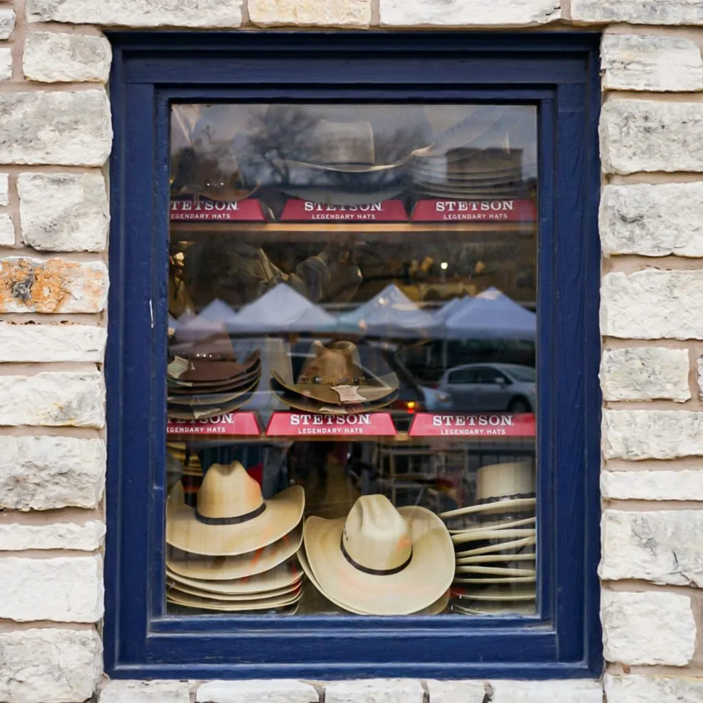 A window display showcases stacked Stetson cowboy hats against a stone wall background.