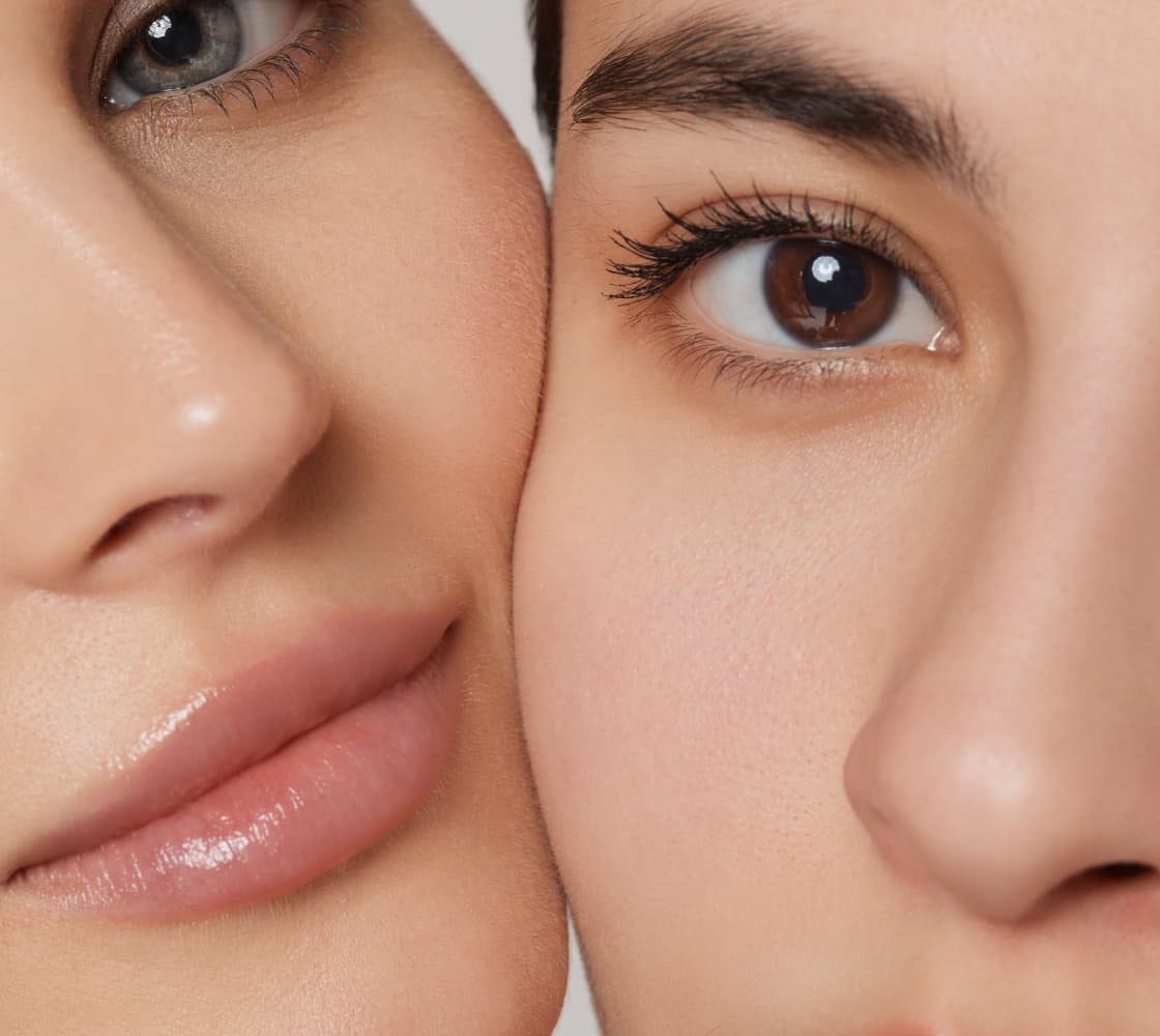 Two close-up female faces side by side, one with a soft smile and slightly parted lips, the other with a neutral expression showcasing large brown eyes and smooth skin.