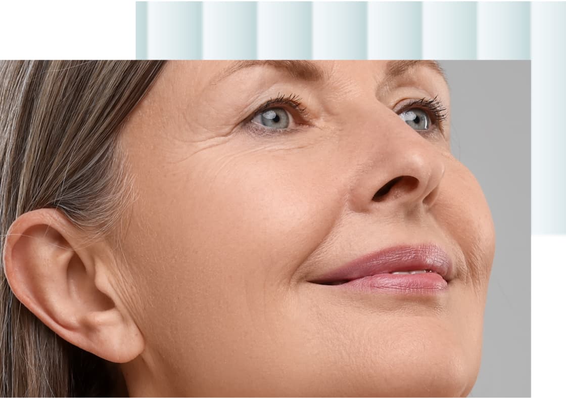 A close-up of a smiling woman with long hair, showing her face and the upper part of her neck. She has light blue eyes and is wearing minimal makeup, with a natural look.