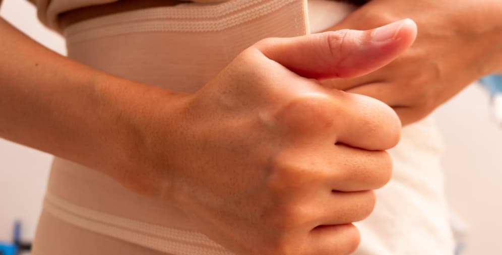 A close-up of a hand giving a thumbs up gesture, showing a beige band wrapped around the torso.