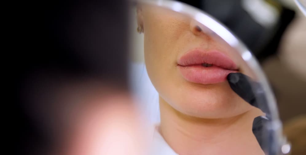 A close-up of a person's lips being examined in a mirror, showing full lips and a finger gently touching the lower lip.
