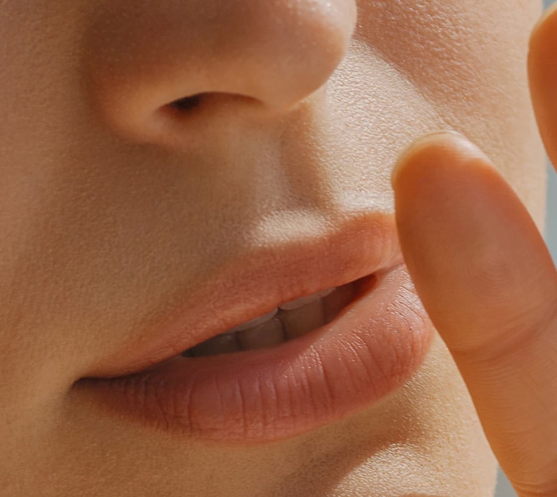 A close-up of a person's face focusing on the lips and a hand gently touching the mouth, suggesting a 'shh' gesture.