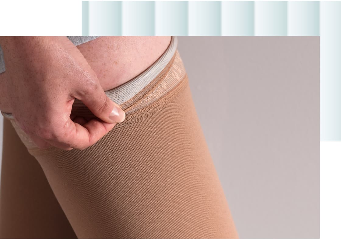 A person adjusting the waistband of tan-colored hosiery on their thigh.