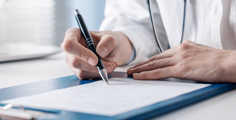 A person's hand holding a pen, writing on a piece of paper placed on a clipboard.