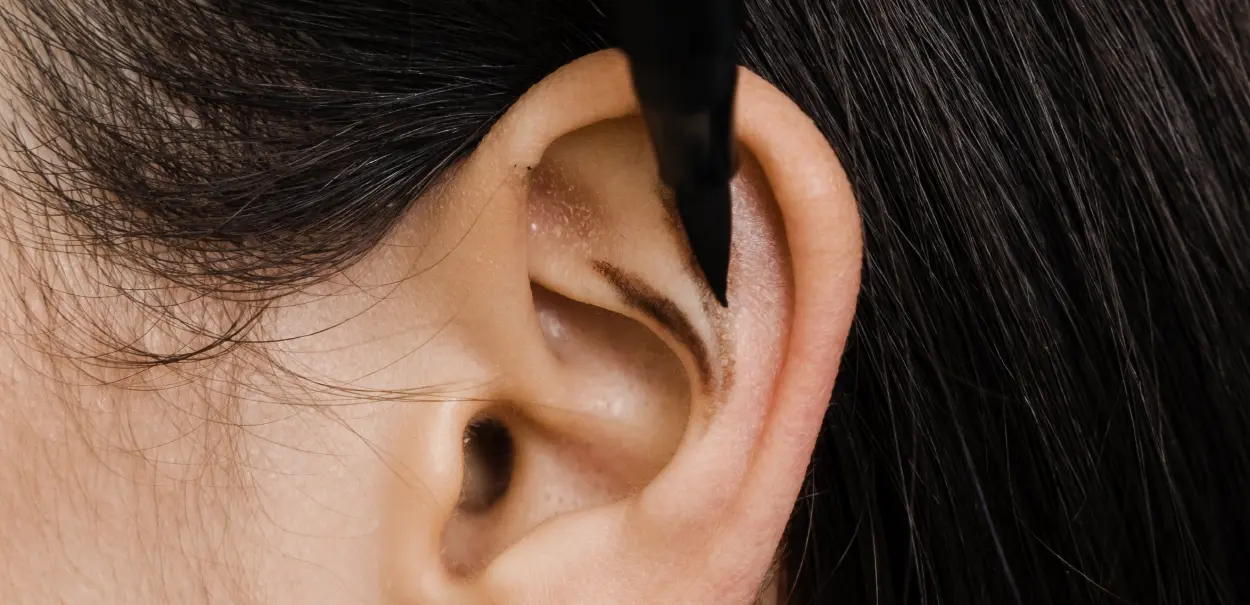 A close-up image of a human ear with a black pen pointing towards the ear canal.