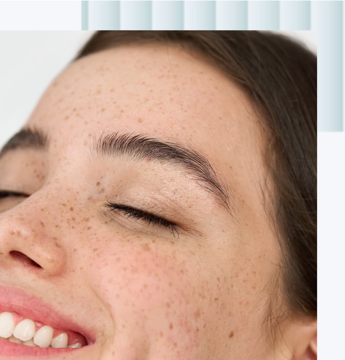A close-up of a smiling young woman with freckles, eyes closed and a natural look.
