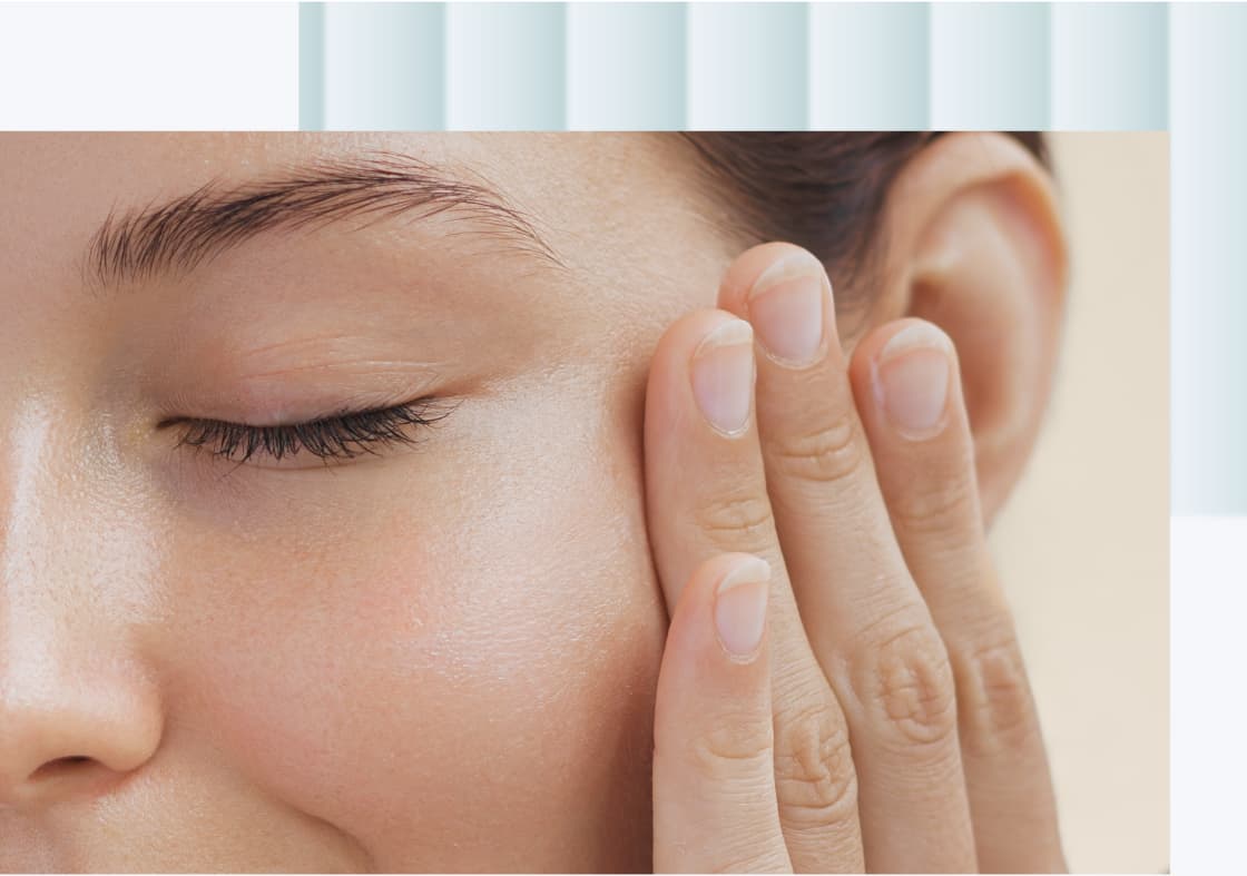 A close-up of a woman touching her cheek with one hand, eyes closed and a gentle expression on her face.