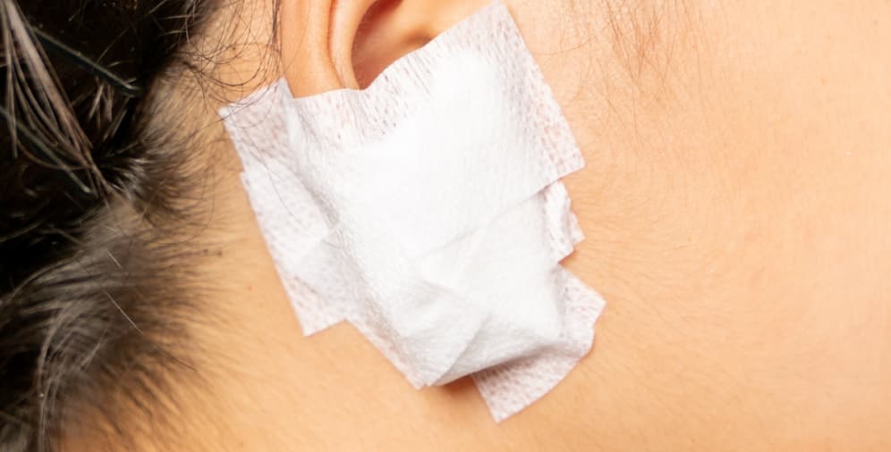 A large, white adhesive bandage applied to the skin behind the ear.