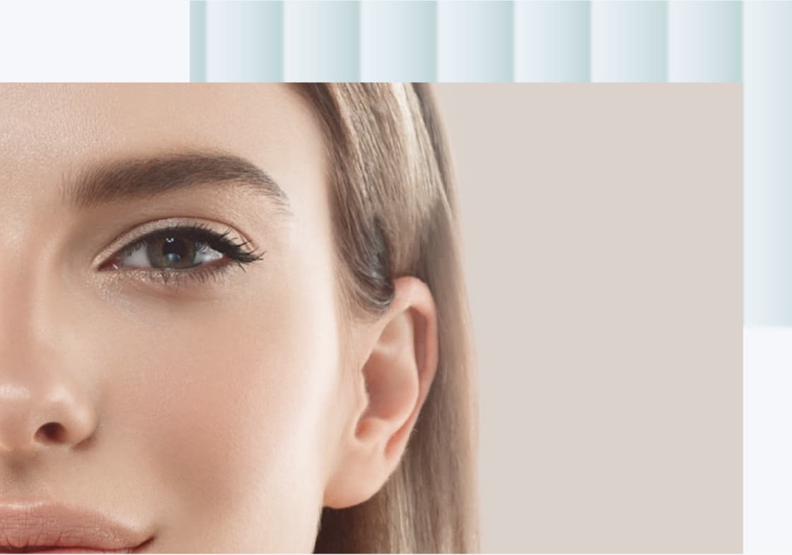 A close-up image of a woman's face, primarily focusing on her eye and a portion of her smile. She has natural makeup, with well-defined lashes and smooth skin. Her hair is light brown and falls softly around her face.