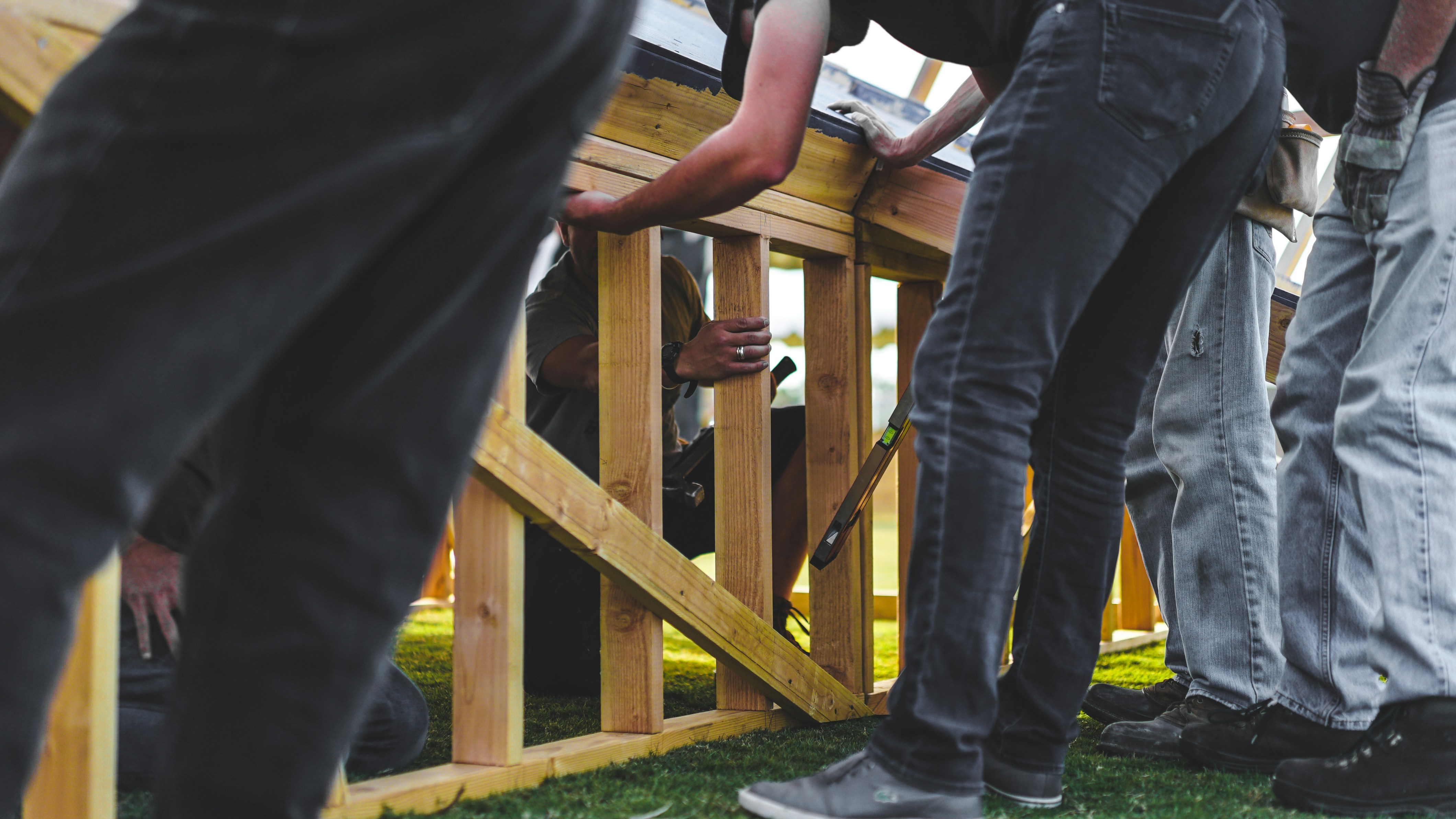 Workers installing a wooden fence outdoors, positioning support posts and securing the frame during the construction process.