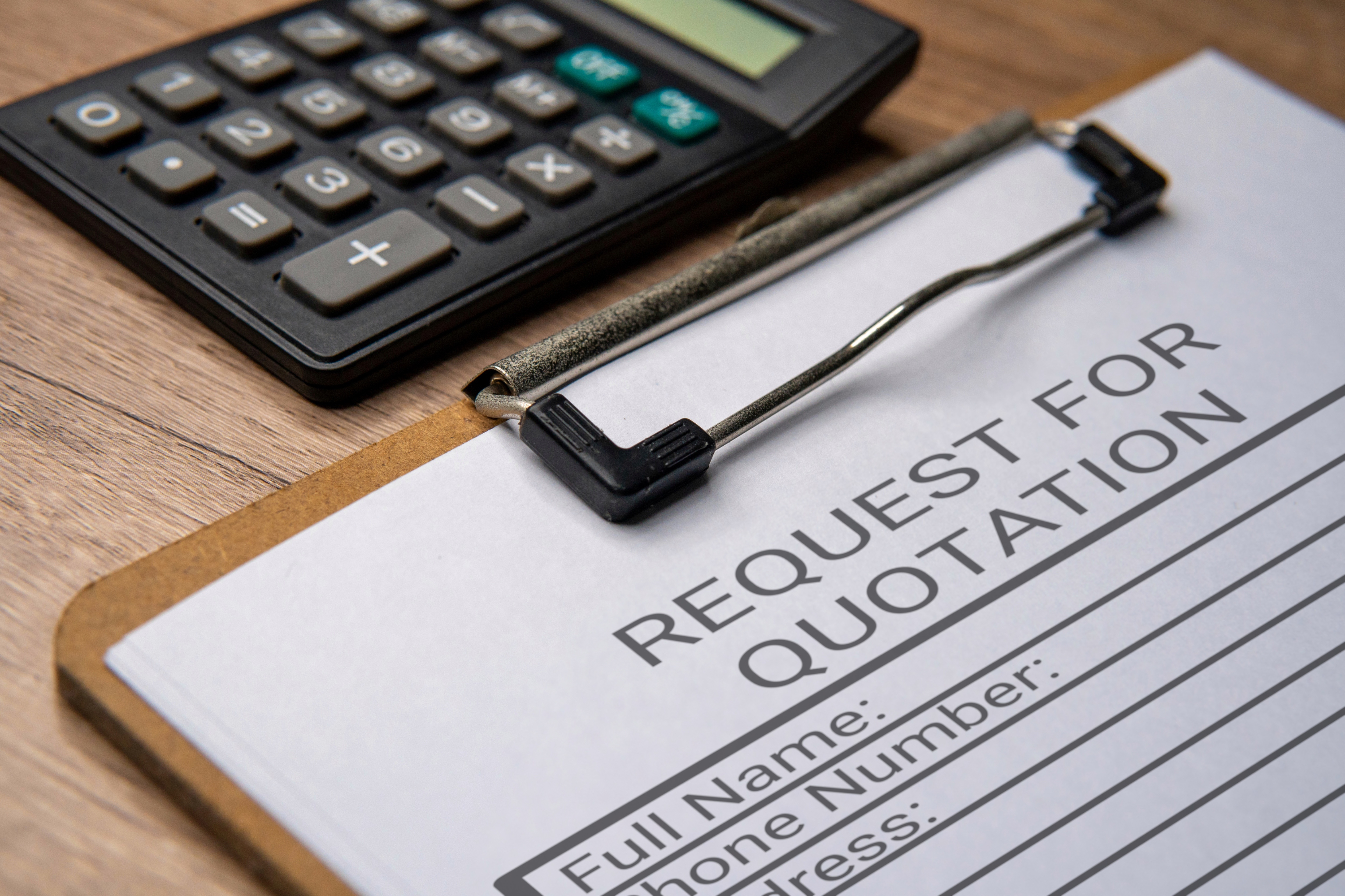 Close-up of a clipboard holding a “Request for Quotation” form on a wooden desk, with a calculator beside it.