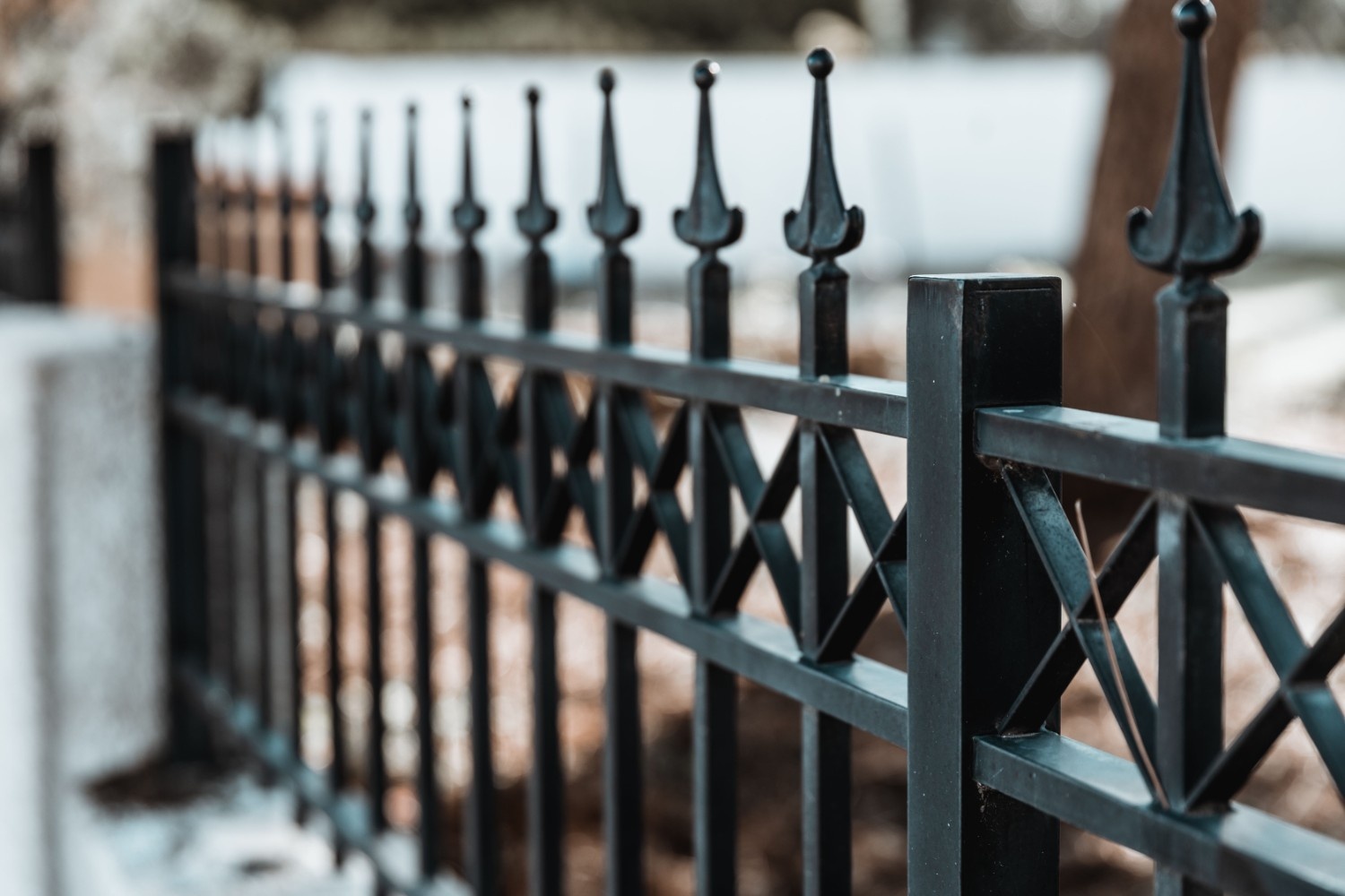 Black wrought-iron fence with decorative spear finials and a blurred residential background.