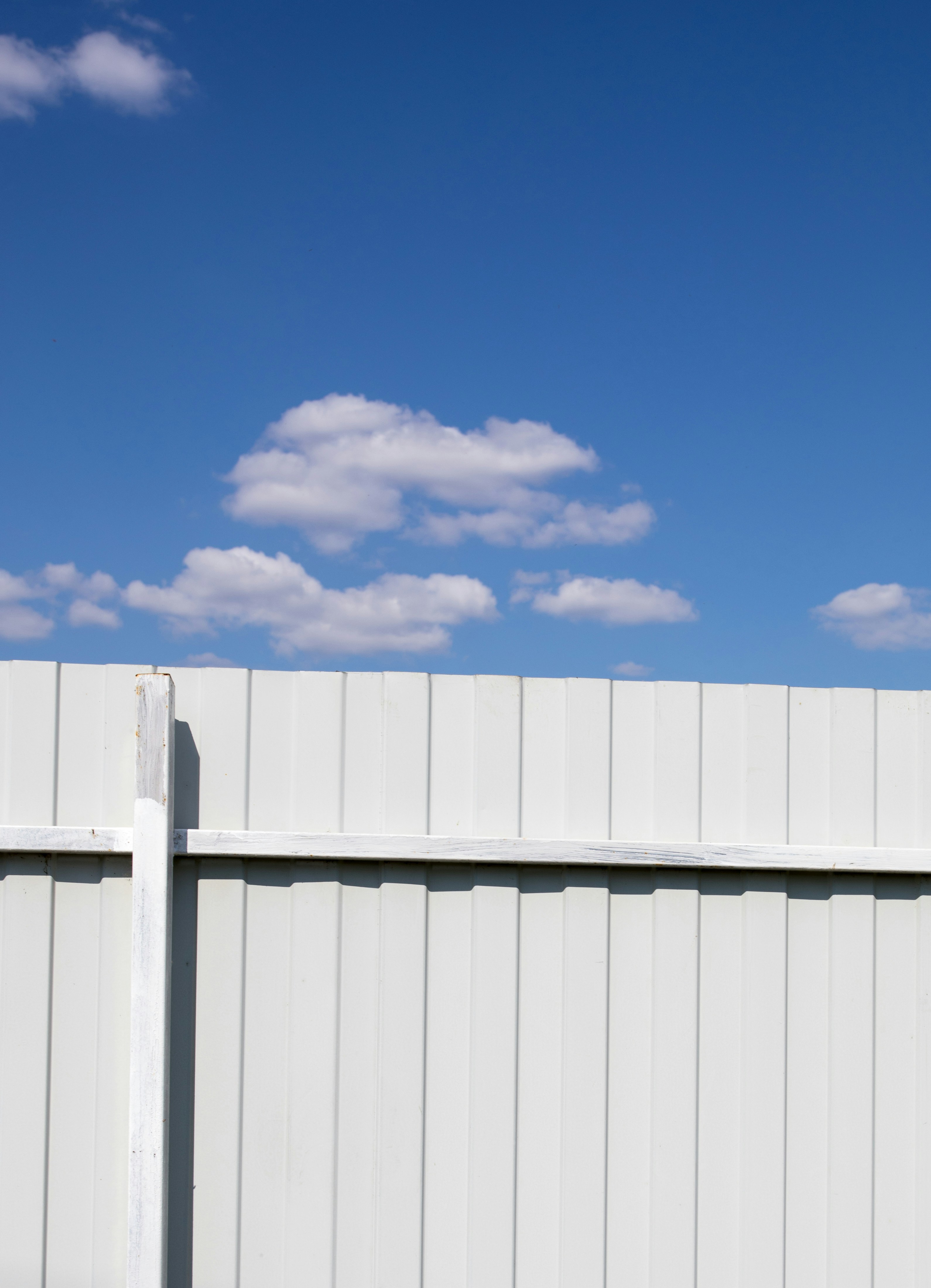 Clean white vinyl fence with soft clouds in a bright blue sky