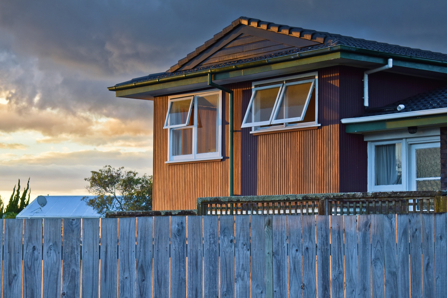 House with wood-slat siding behind a wooden fence at dusk.