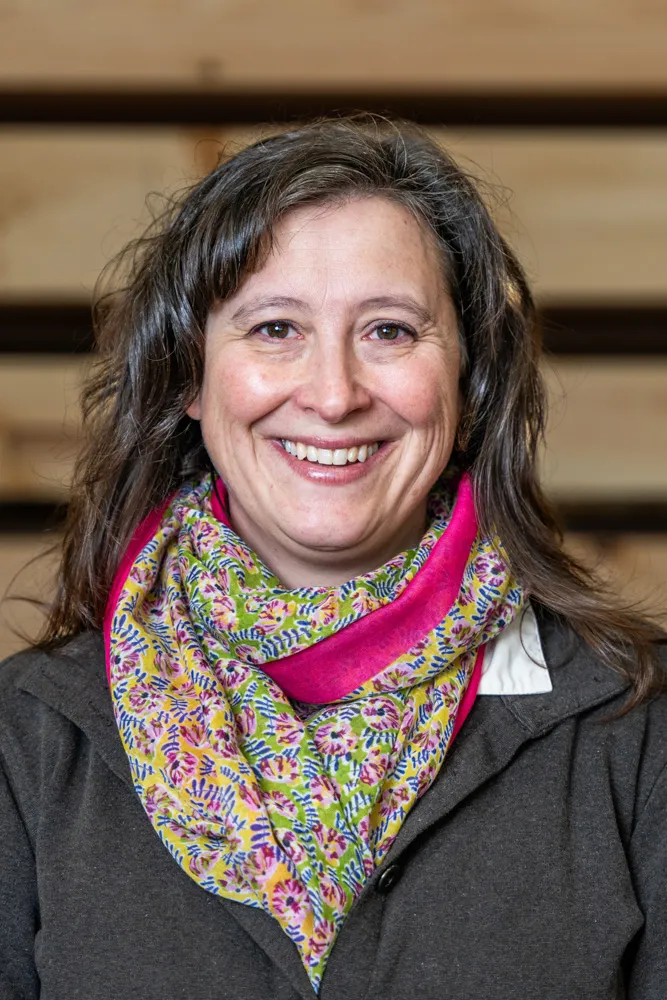 Woman smiling warmly, wearing colorful scarf against wooden background