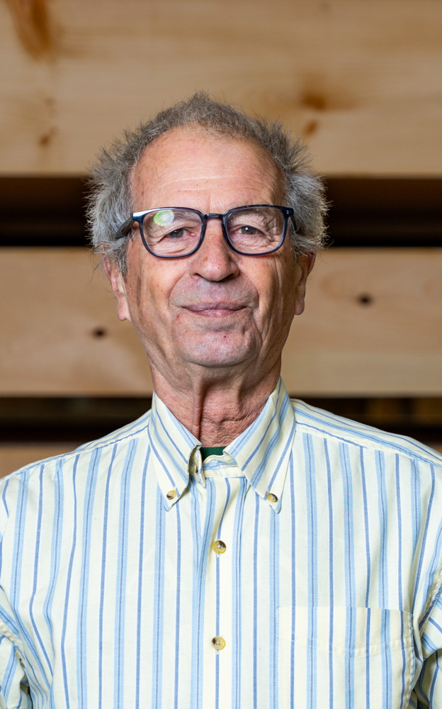 Elderly man with glasses smiling, wearing blue and white striped shirt