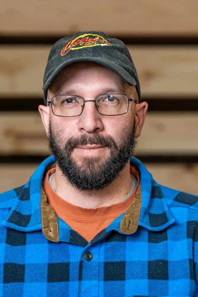 Man in blue plaid shirt and baseball cap wearing glasses