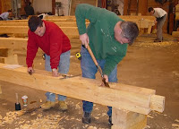 Two woodworkers in colorful clothing working on a large wooden board in workshop