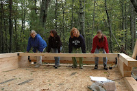 Four people sitting on wooden bench in forest clearing outdoors