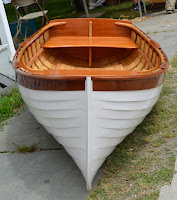 Wooden and white rowboat viewed from above, displayed on pavement outdoors