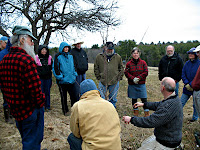 Group of people gathered outdoors in winter clothing planting or tending to a young tree