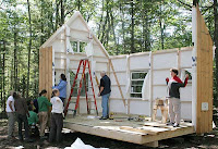 Group of people building or constructing a small wooden structure in forest clearing.