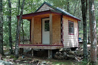 Wooden cabin on stilts in forest surrounded by tall trees and greenery