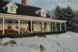 White farmhouse with columns and snow-covered front yard during winter
