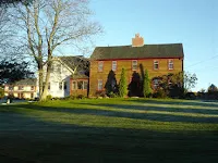 Yellow brick church building with steeple on grassy grounds, bare trees nearby