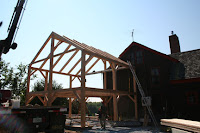 Wooden timber frame structure under construction with existing stone building