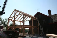 Wooden timber frame structure under construction with existing stone building