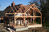 Wooden frame house under construction with exposed timber trusses against blue sky
