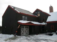 Black barn with red garage door in snowy winter landscape