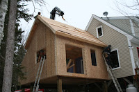 House under construction with wooden framing and partially installed siding and windows.