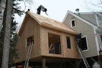 House under construction with wooden framing and partially installed siding and windows.