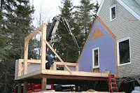Blue house structure being loaded onto truck with wooden framework support