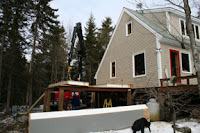 A two-story house under construction surrounded by tall evergreen trees and construction equipment.