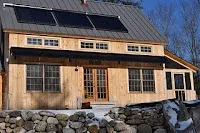 Modern farmhouse with solar panels on dark roof and stone foundation wall.