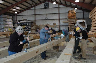 Group of workers in hard hats measuring wooden beams in an industrial warehouse