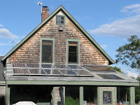 Two-story brick house with white shutters and covered porch under blue sky.